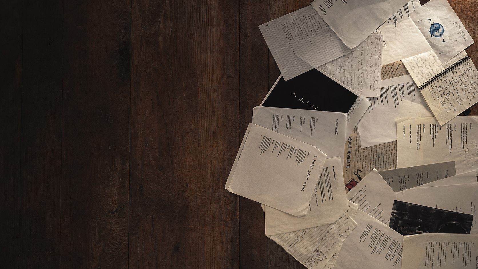 Aston River lyric sheets, handwritten drafts, notebooks and printed songs spread across a wooden table.